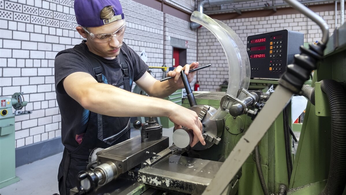 Luca spannt das Werkstück ein und trägt dabei eine Schutzbrille. 