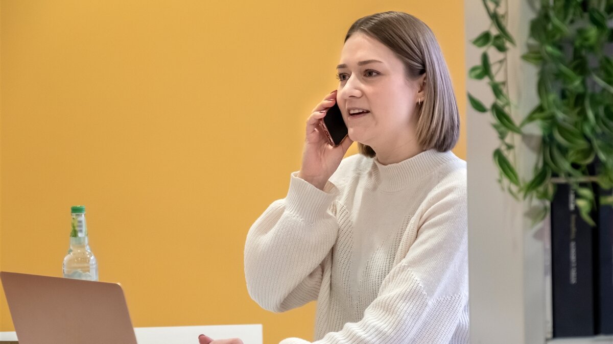 Eine junge Frau sitzt am Laptop und telefoniert.