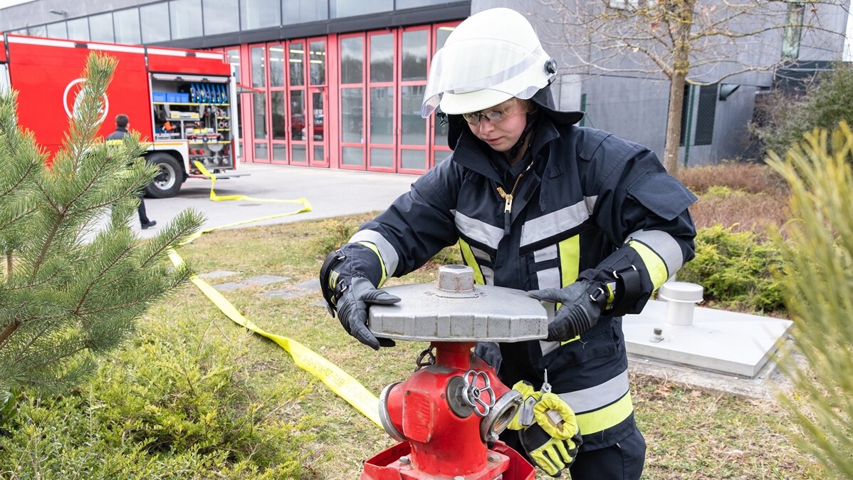 Eine junge Frau in Feuerwehruniform und Handschuhen und Helm arbeitet an einem Hydranten.