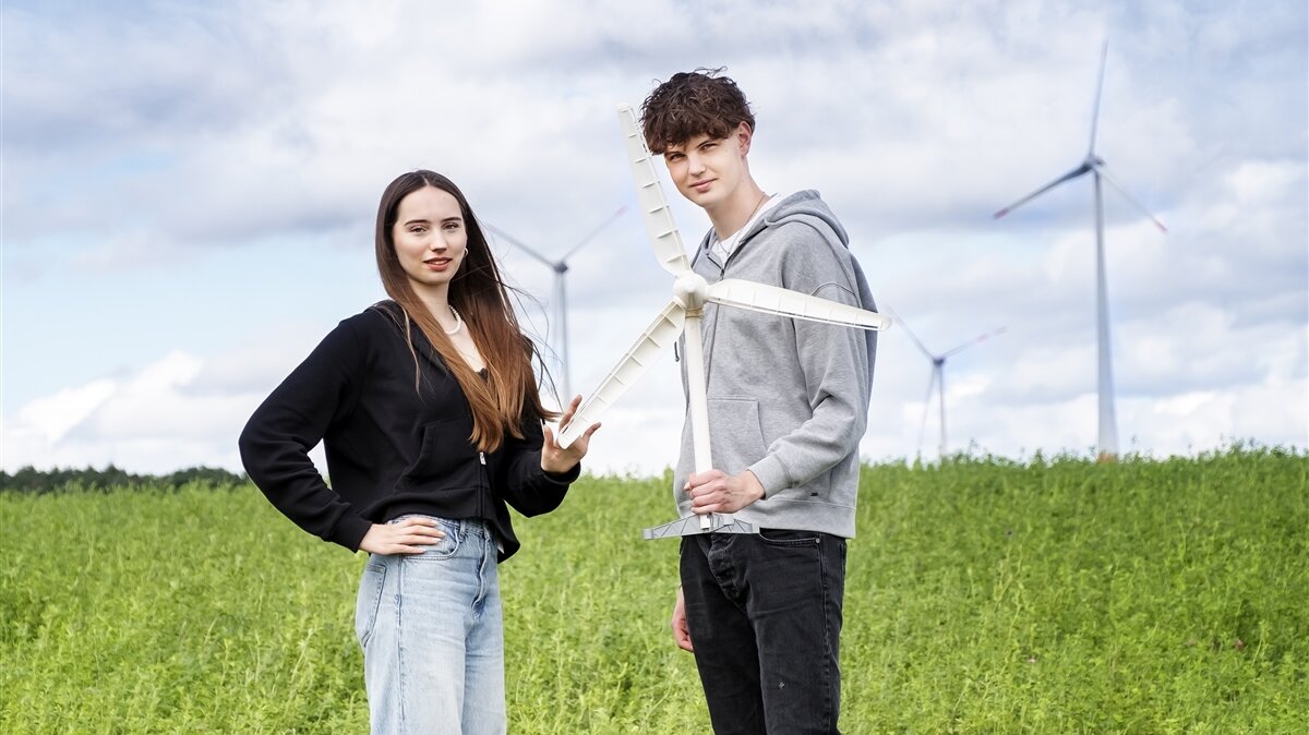 Zwei Jugendliche stehen auf einer Wiese vor Windrädern.
