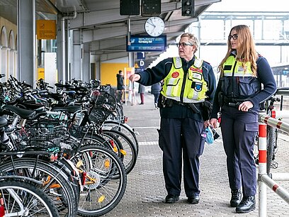 Zwei Frauen in Wachschutzkleidung stehen am Bahnhof.