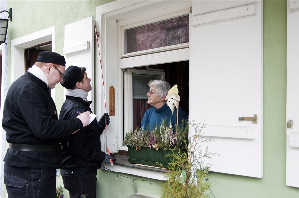 Zwei Schornsteinfeger vor dem Haus einer älteren Dame.