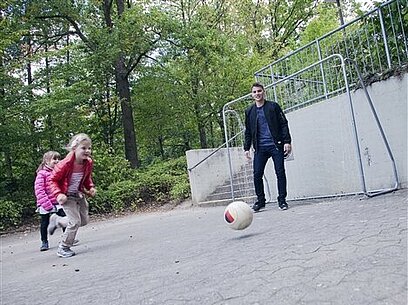 Ein Erzieher spielt mit zwei Mädchen Fußball.