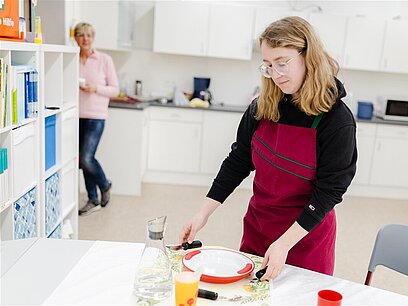 Eine junge Frau mit Schürze deckt einen Tisch.