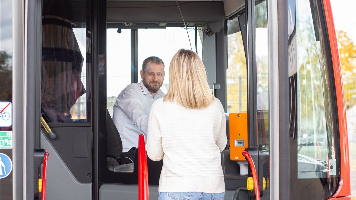 Eine junge Frau spricht im Bus mit dem Busfahrer und kauft dabei ein Ticket.