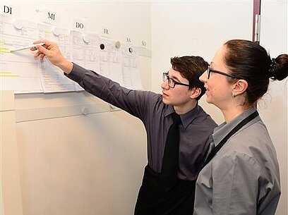 Ein junger Mann und eine junge Frau besprechen ihren Arbeitseinsatz anhand eines Dienstplans.