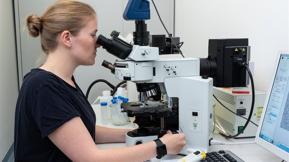Eine junge Frau schaut sich Proben unter einem Mikroskop an.