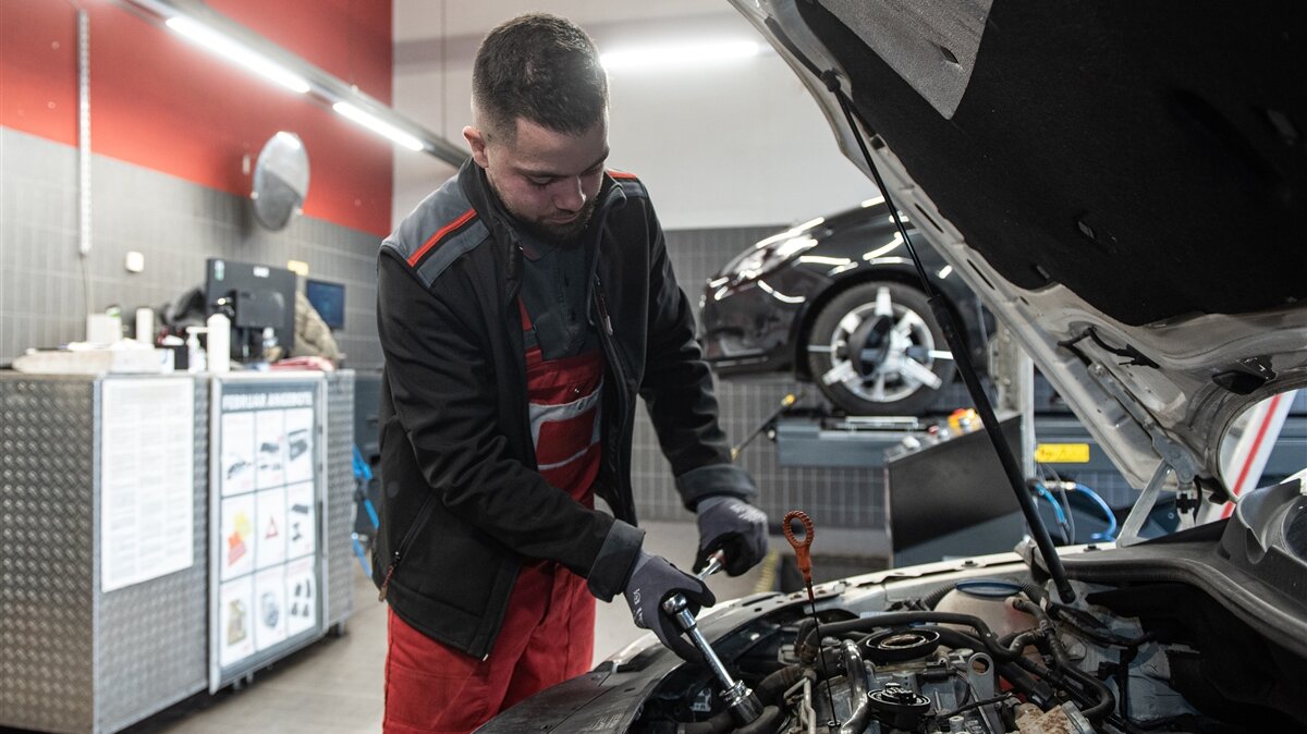 Ein Mann mit Handschuhen arbeitet mit einem Steckschlüssel an einem Motor in einer Werkstatt.