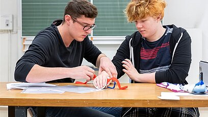 Zwei junge Männer unterhalten sich in einem Klassenzimmer.