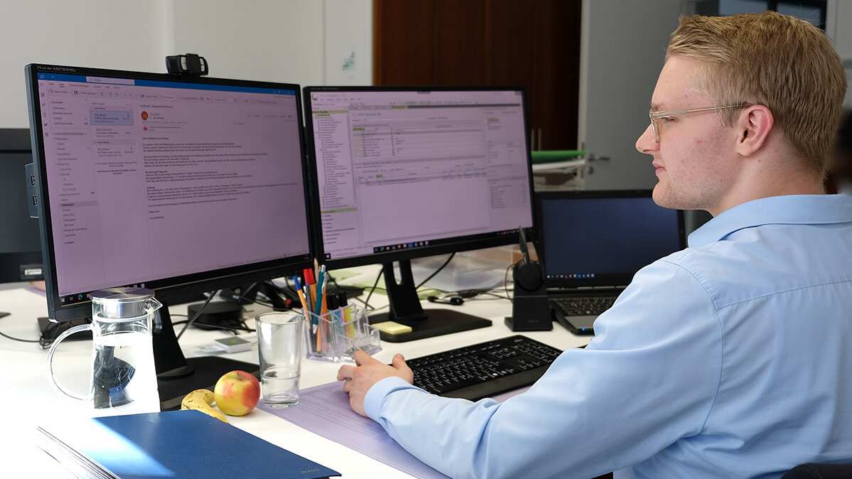 Jonas sitzt im Büro am Computer und liest E-Mails.