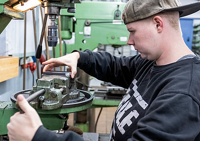 Eine junge Frau spannt ein Metallstück in einen Schraubstock.