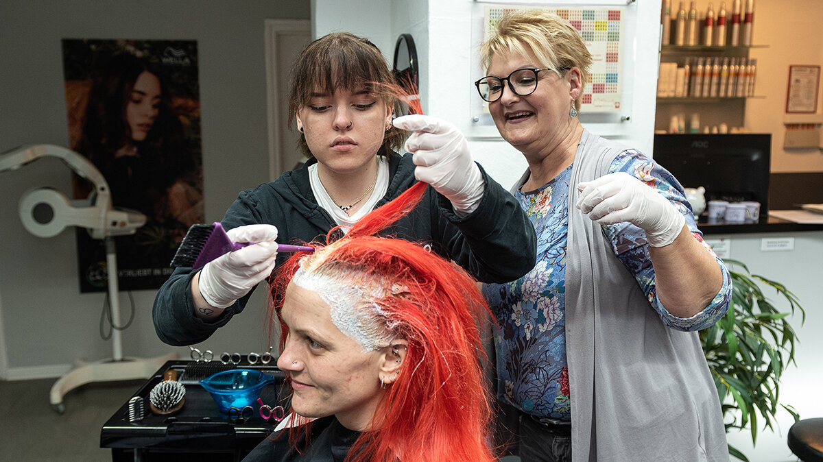 Eine Ausbildern leitet eine Auszubildende beim Färben von Haaren an.