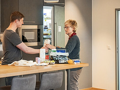 Ein junger Mann hilft einer Frau dabei, Lebensmittel in den Kühlschrank zu räumen.