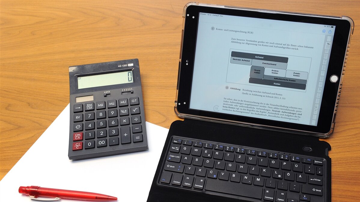 Ein Laptop und ein Taschenrechner und ein Block mit Stift auf einem Tisch.