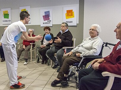 Eine Frau macht Bewegungsübungen mit einer Gruppe von älteren Menschen in einem Pfegeheim.