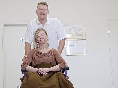 Eine Pflegekraft schiebt eine Frau im Rollstuhl.
