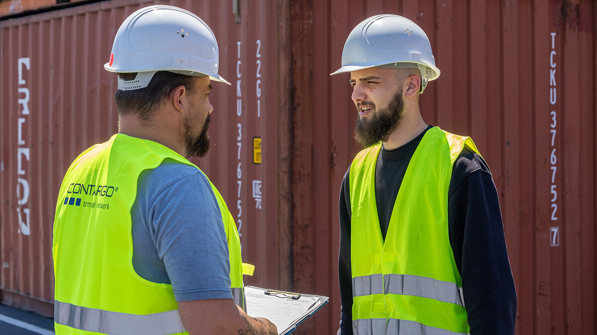 Noah und sein Vorarbeiter besprechen sich vor einem Container auf dem Hafengelände.