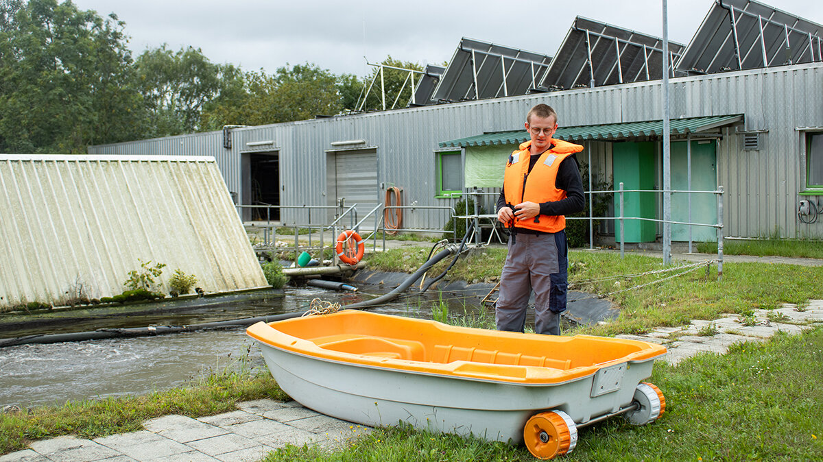 Luis trägt eine Schwimmweste und bereitet das Boot für die Reparatur auf dem Becken vor.