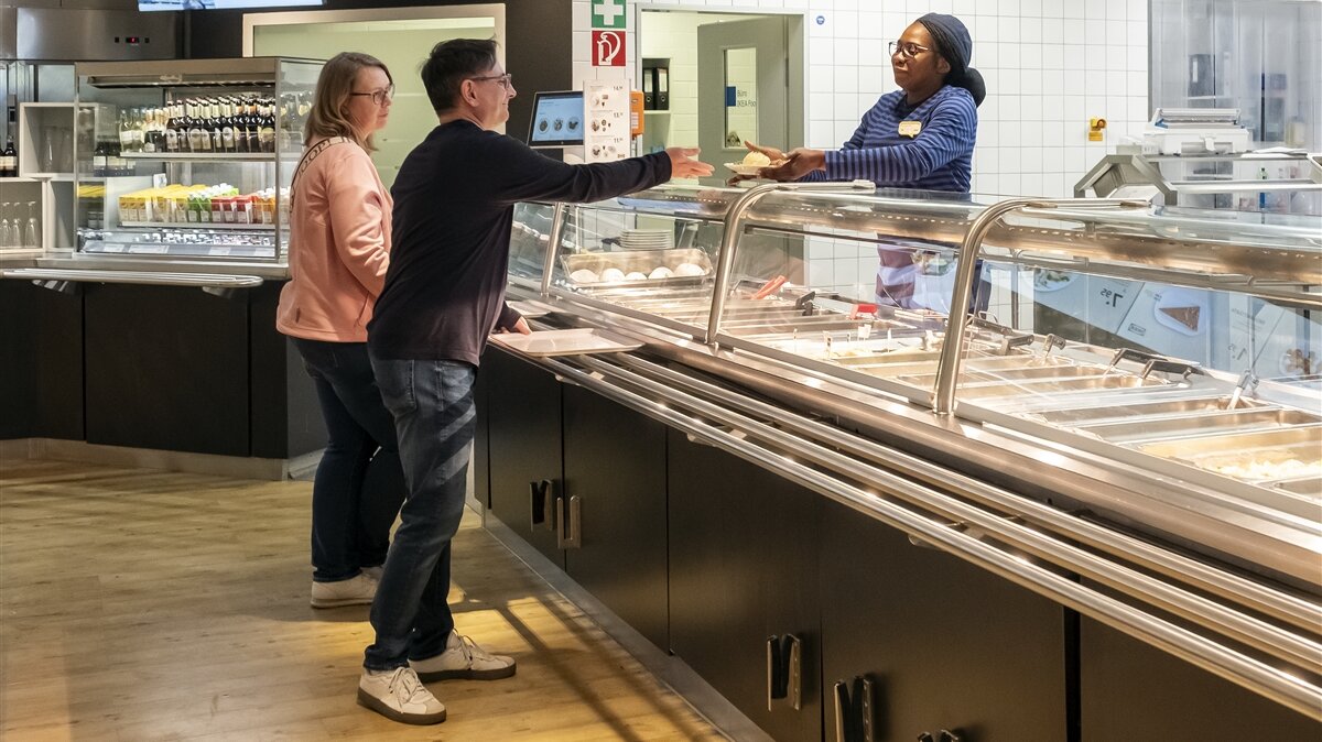 Josephat gibt an der Theke Essen an Kundinnen und Kunden aus.