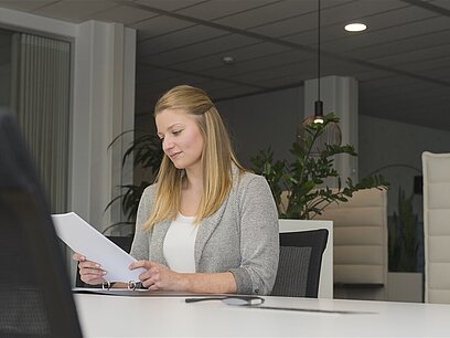 Eine junge Frau sitzt an einem Tisch und schaut sich Dokumente an.