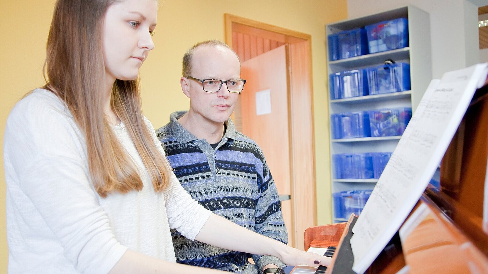 Ein Musiklehrer überprüft den Lernerfolg einer Klavierschülerin.