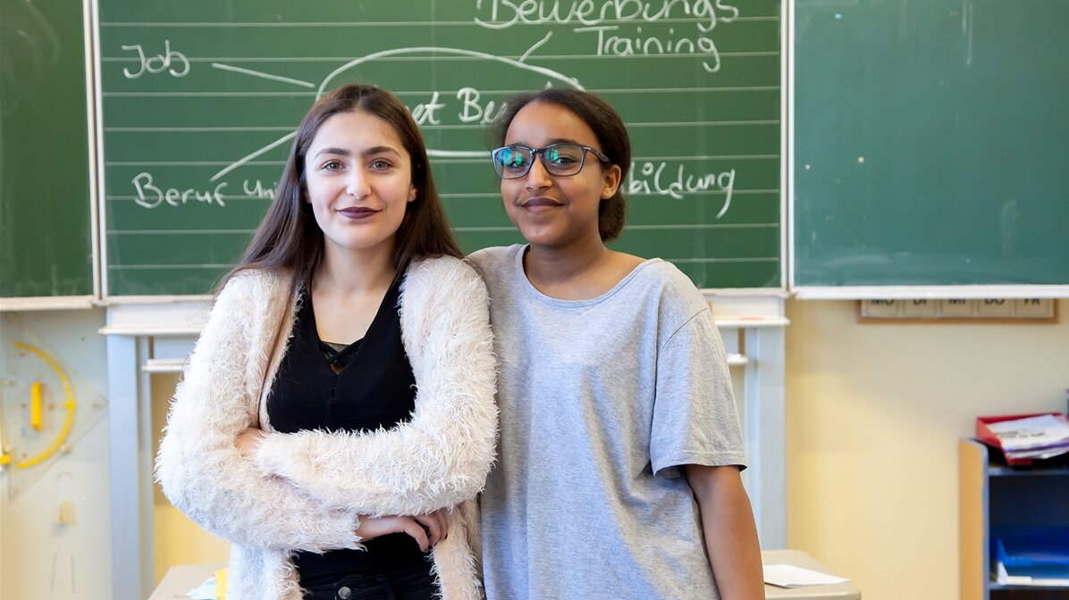 Zwei Schülerinnen stehen vor der Tafel im Klassenzimmer.