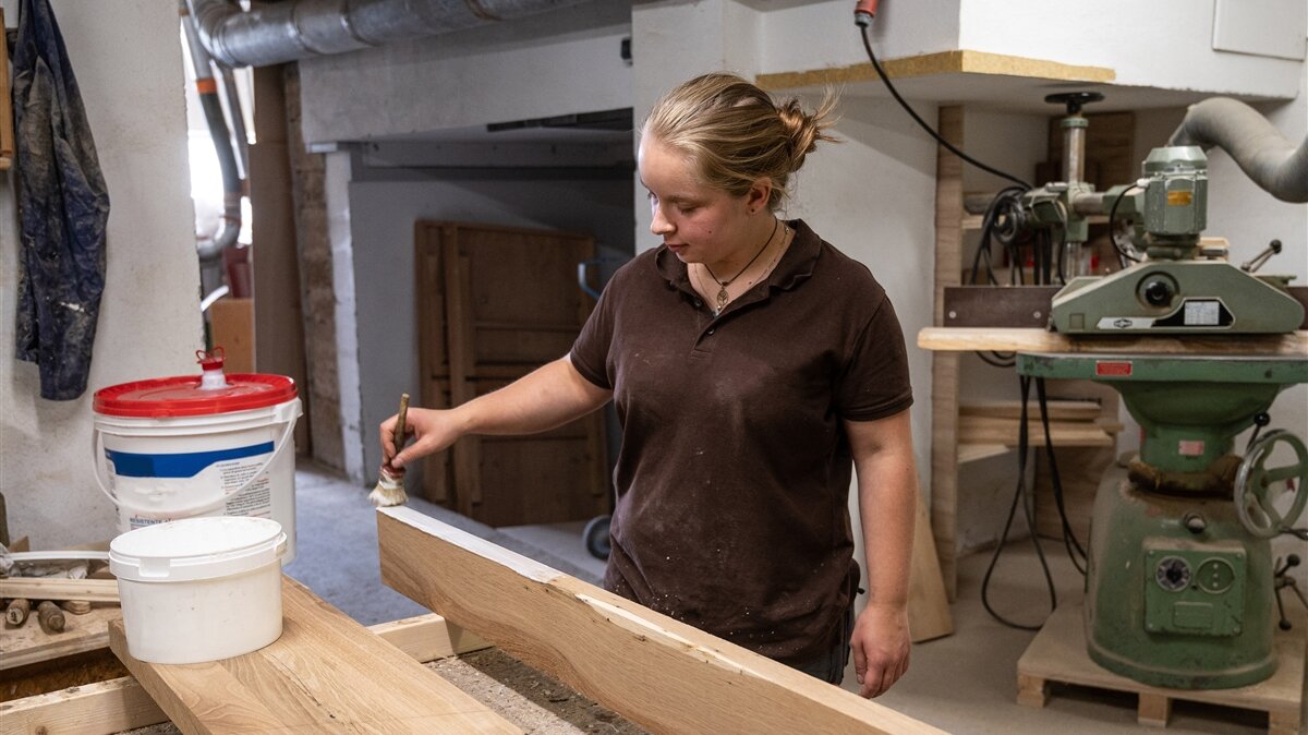 Eine Frau verleimt die Oberfläche eines Holzstücks.