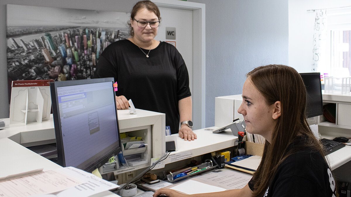 Yasmina sitzt an der Anmeldung und nimmt eine Patientin an.