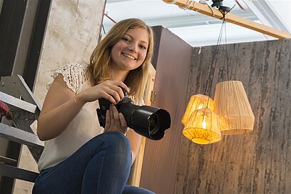 Eine junge Frau sitzt auf einer Treppe und hält eine Kamera in den Händen.