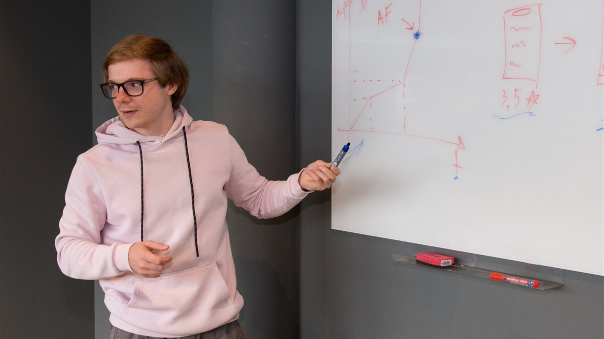 Ein junger Mann steht mit einem Stift in der Hand vor einem Whiteboard und schaut ins Publikum.