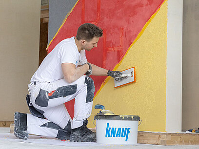 Franz glättet die Farbe auf einer Mauer.