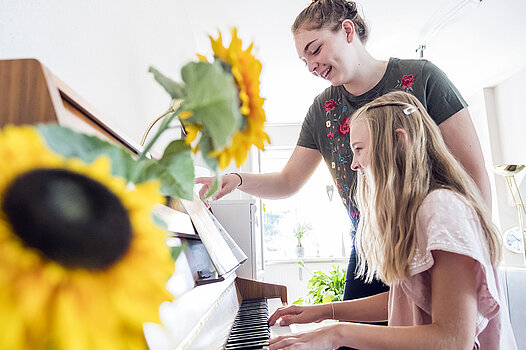 Eine junge Frau gibt einem Mädchen Klavierunterricht.
