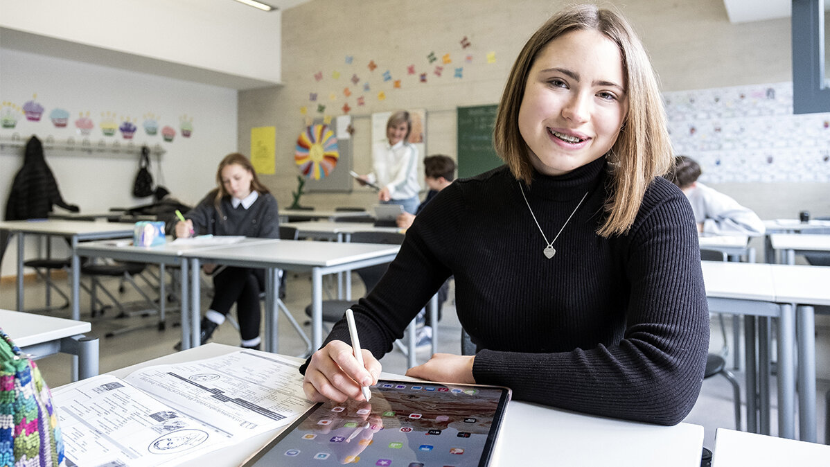Eine Schülerin lächelt und sitzt vor einem Tablet.