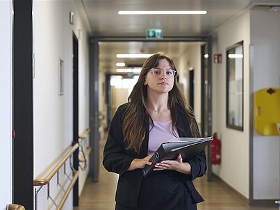 Eine junge Frau läuft mit einer Akte in der Hand Richtung Kamera.