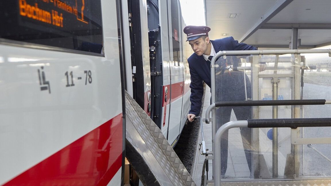 Ein junger Mann fährt eine Rollstuhlrampe an die Tür eines Zuges.