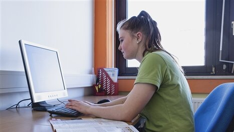 Eine junge Frau sitzt am Schreibtisch und arbeitet am Computer.