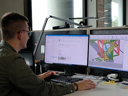 60 Ein junger Mann sitzt vor einem Computer und arbeitet in einem Programm an einem 3D-Modell.