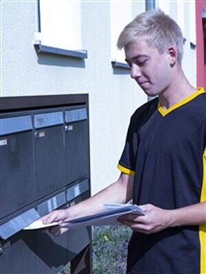Ein Jugendlicher wirft Briefe in einen Briefkasten.