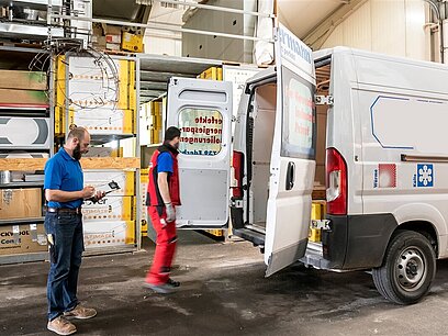 Zwei Männer bereiten das Verladen von Ware in einen geöffneten Sprinter vor.