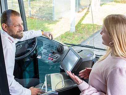 Eine junge Frau unterhält sich im Bus mit dem Busfahrer.