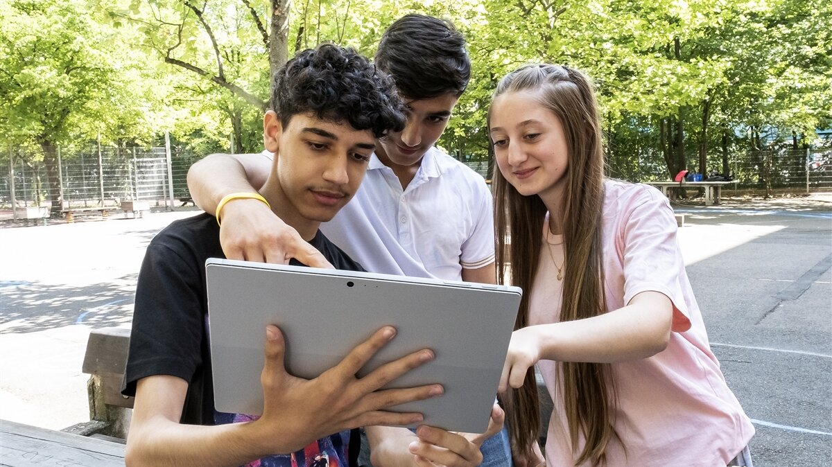 Auf dem Pausenhof schauen drei Jugendliche konzentriert in ein Tablet.