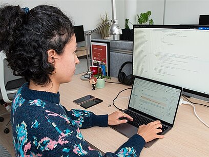 Eine junge Frau arbeitet in einem Büro am PC.