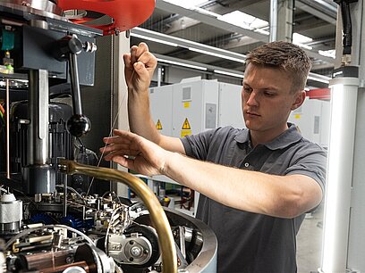 Ein junger Mann kontrolliert Maschinen und Anlagen im Technikraum.