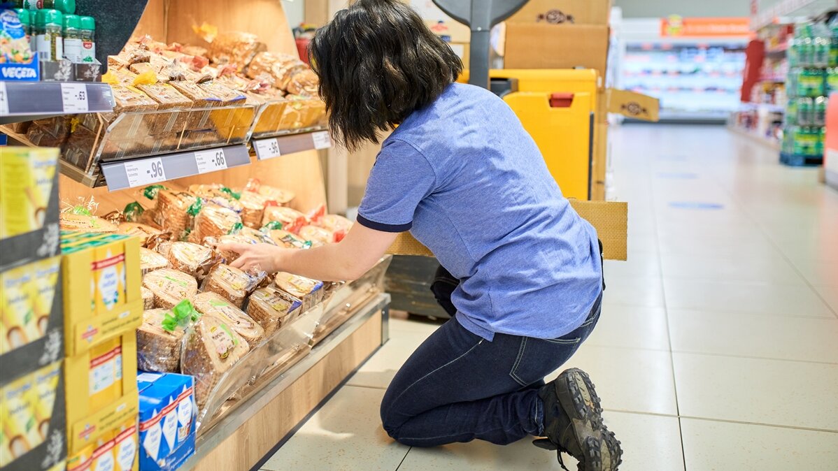 Eine Frau räumt Waren in ein Supermarkt-Regal ein.