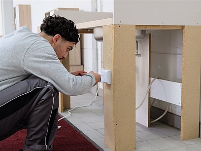 Ein junger Mann schraubt mit einen Handschraubenzieher eine Anschlussdose auf.