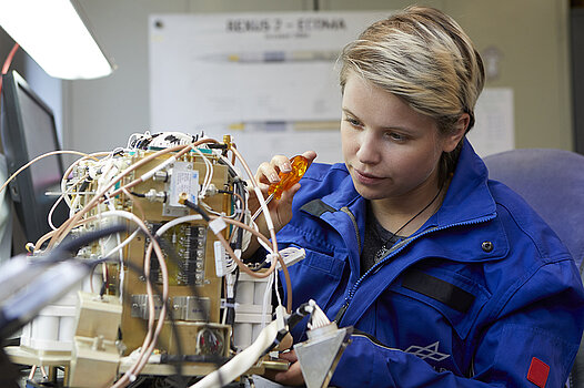 Eine junge Frau arbeitet mit einem Schraubenzieher an einem elektrischen Gerät.