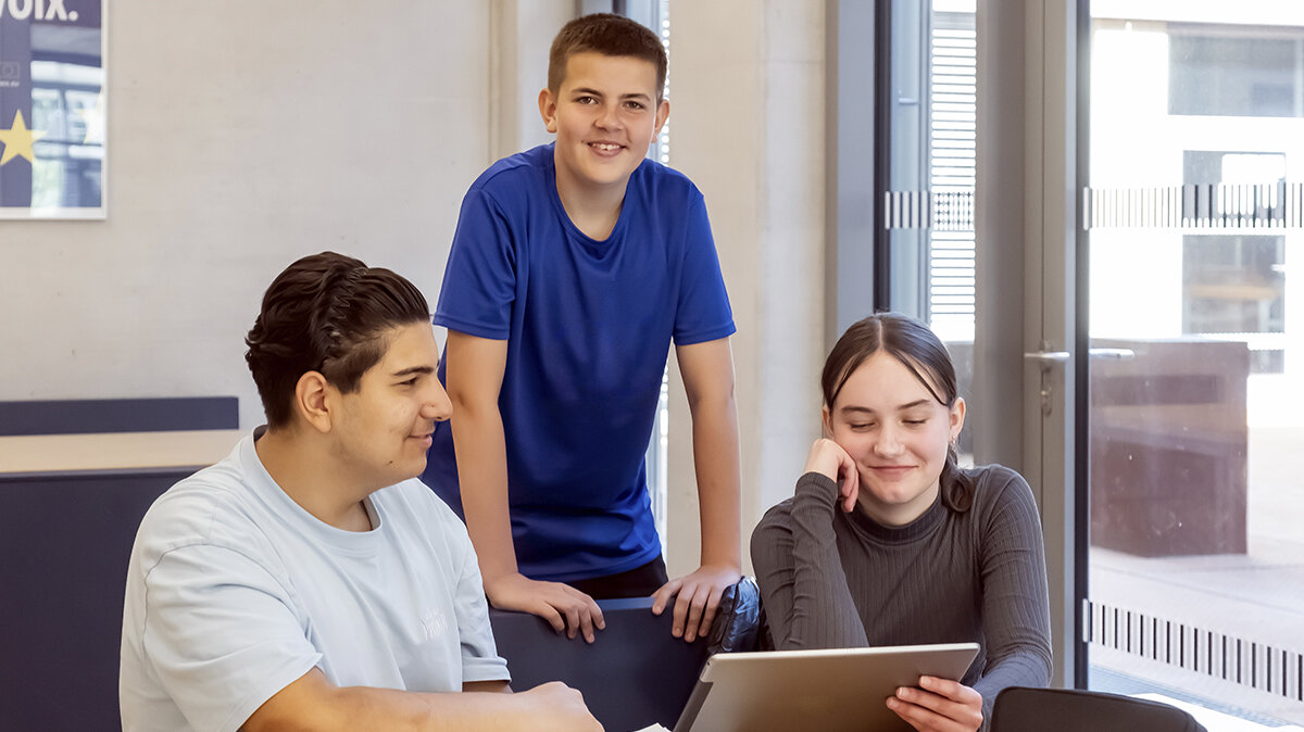 Zwei Schülerinnen und ein Schüler schauen gemeinsam auf ein Tablet.