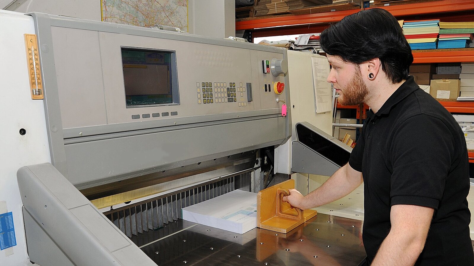 Ein Mann schneidet mit einer Schneidemaschine Druckerzeugnisse zu. 