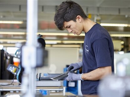 Ein junger Mann arbeitet mit Schutzhandschuhen an einem Metallstück.