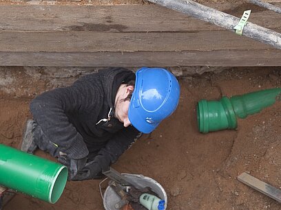 Ein junger Mann mit Helm bereitet auf einer Baustelle ein Rohr zum Verlegen vor.